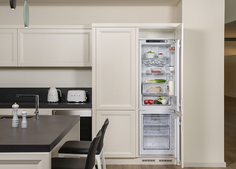 Cucina contemporanea di colore bianco con isola. Sul top cucina sono esposti il bollitore e tostapane Smeg di colore bianco. A destra vi è un frigorifero da incasso combinato con l'anta aperta con in mostra gli alimenti organizzati all'interno.