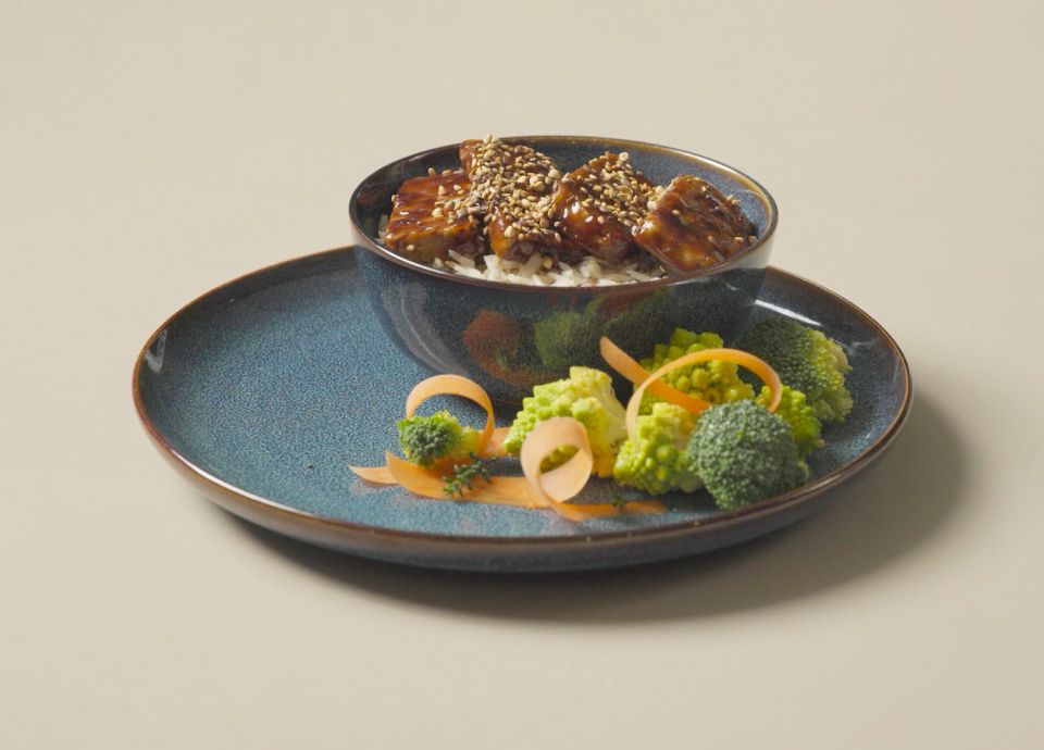 Tofu teriyaki servito con semi di sesamo e verdure su un piatto di ceramica azzurro