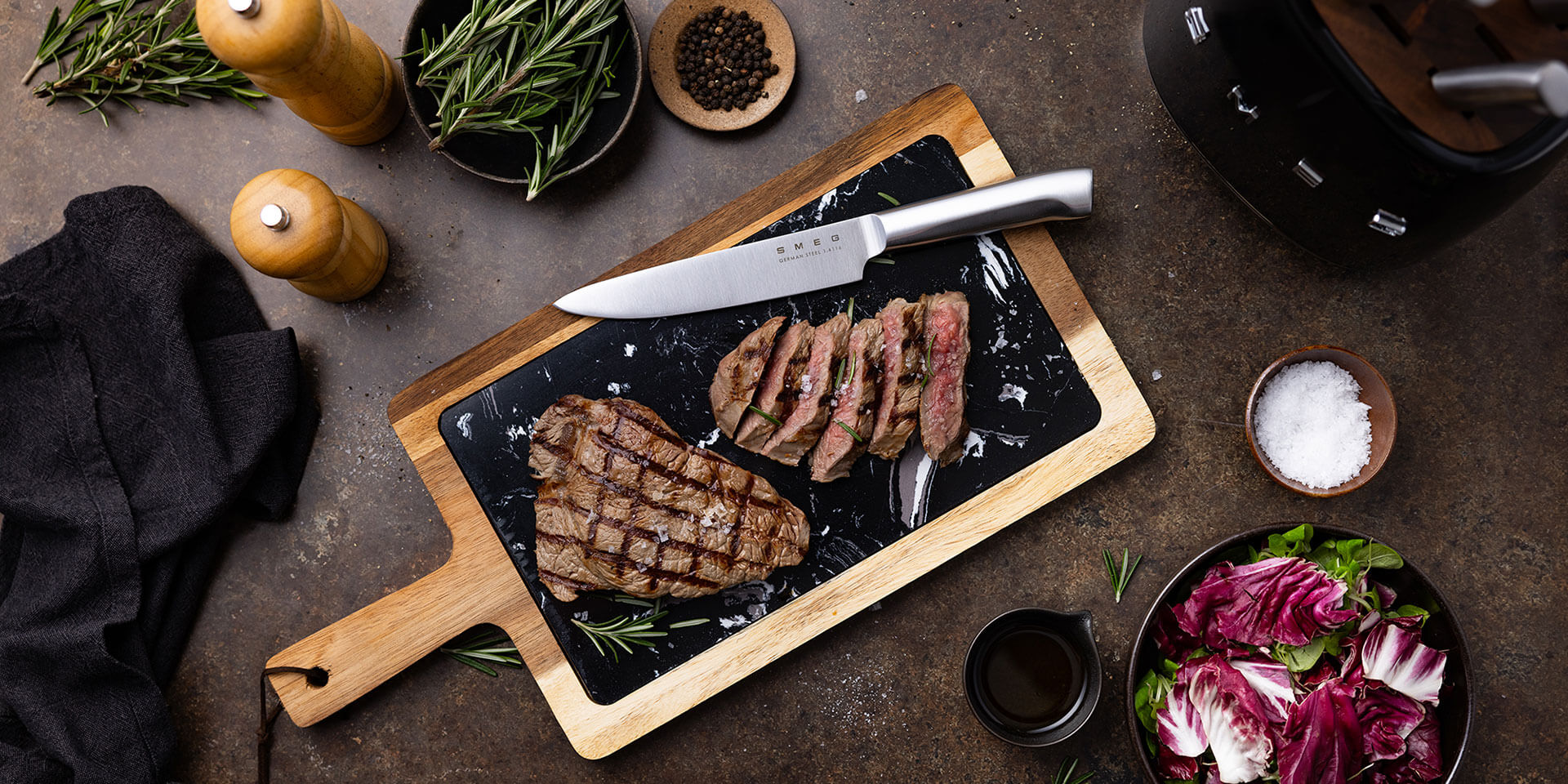 Smeg knife with black knife block and steak on a chopping board