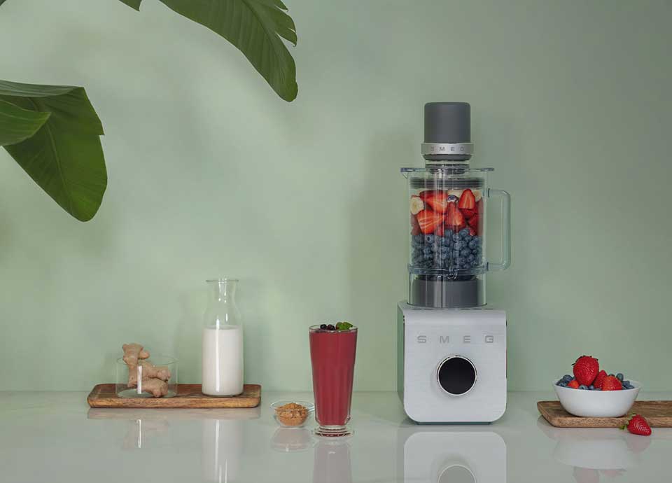 Blender haute performance Smeg avec bol transparent contenant fraises et myrtilles pour smoothie rouge