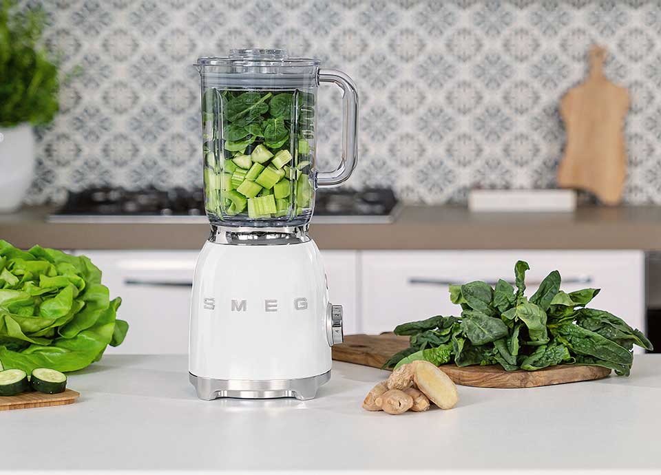 Blender Smeg blanc avec bol contenant épinards et concombre pour smoothie vert détox