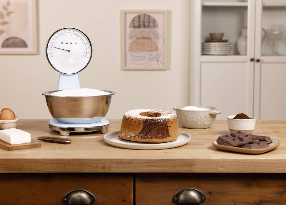 Bilancia da cucina Smeg colore azzurro su un tavolo accanto a una torta