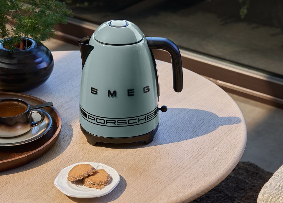 Shade Green Porsche x SMEG kettle on a coffee table with a glass of tea and a cookie