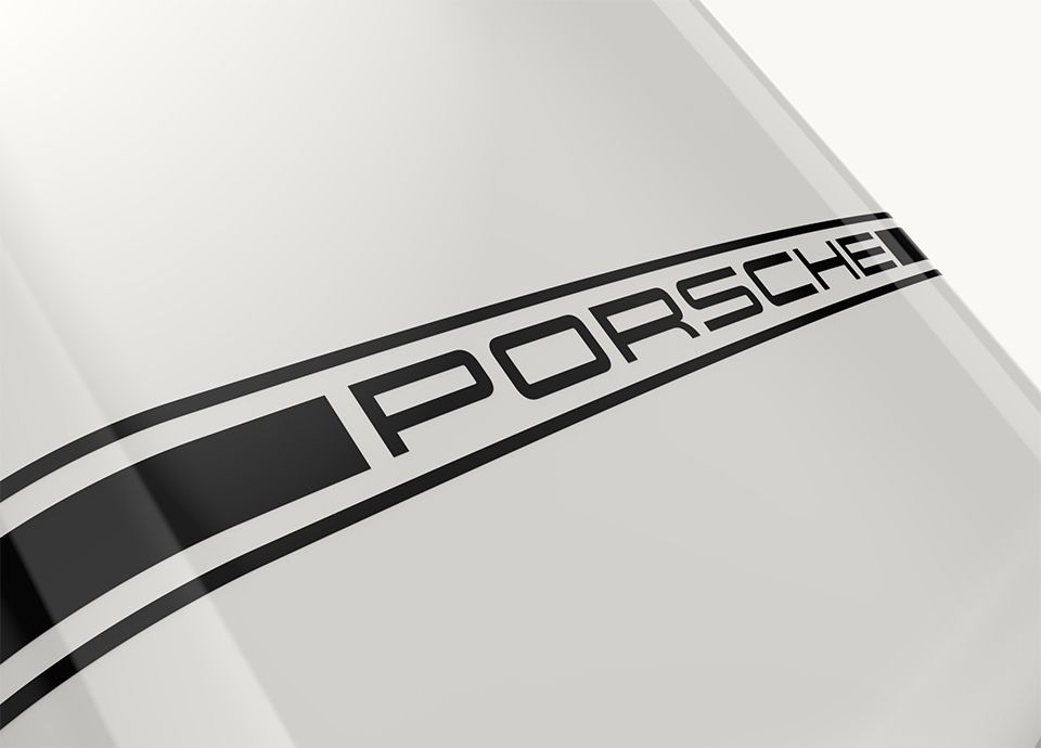 Detail of the front lower part of the refrigerator FAB in colour carrara white. Near the bottom, a horizontal black band features the word "PORSCHE" in black uppercase letters.