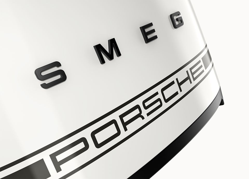 Detail of the front part of the toaster in colour carrara white. The front of the toaster features the brand name "SMEG" in bold uppercase letters, and below it, a second logo reads "PORSCHE", indicating a collaboration between the two brands.