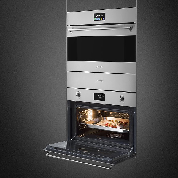 Set composto da abbattitore e forno combinato a vapore Smeg in acciaio inox con vetro nero. Il forno è aperto e al suo interno ci sono delle pietanze in un sacchetto sottovuoto.