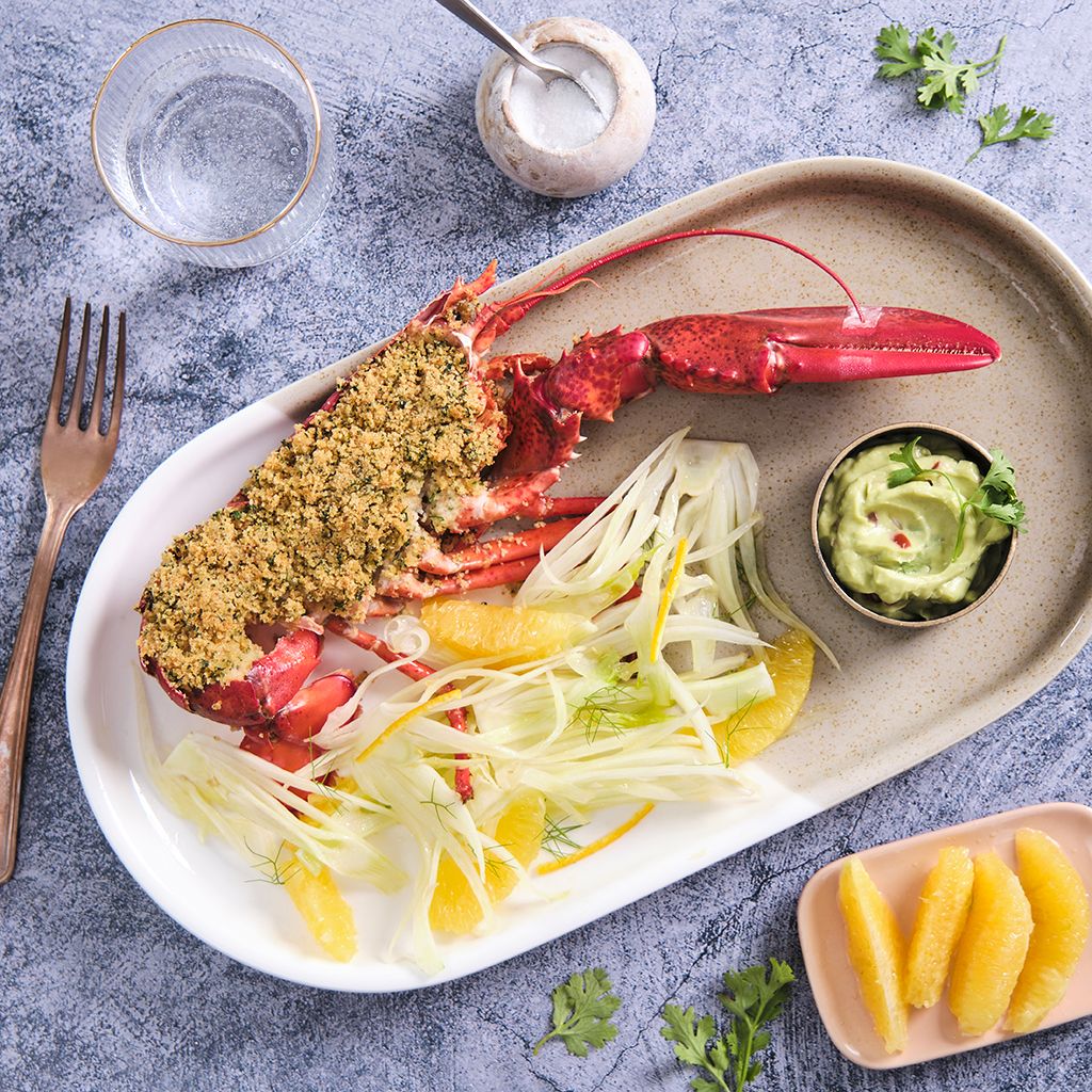 Lobster gratin served with a fresh fennel and orange salad, accompanied by creamy guacamole on a white plate.