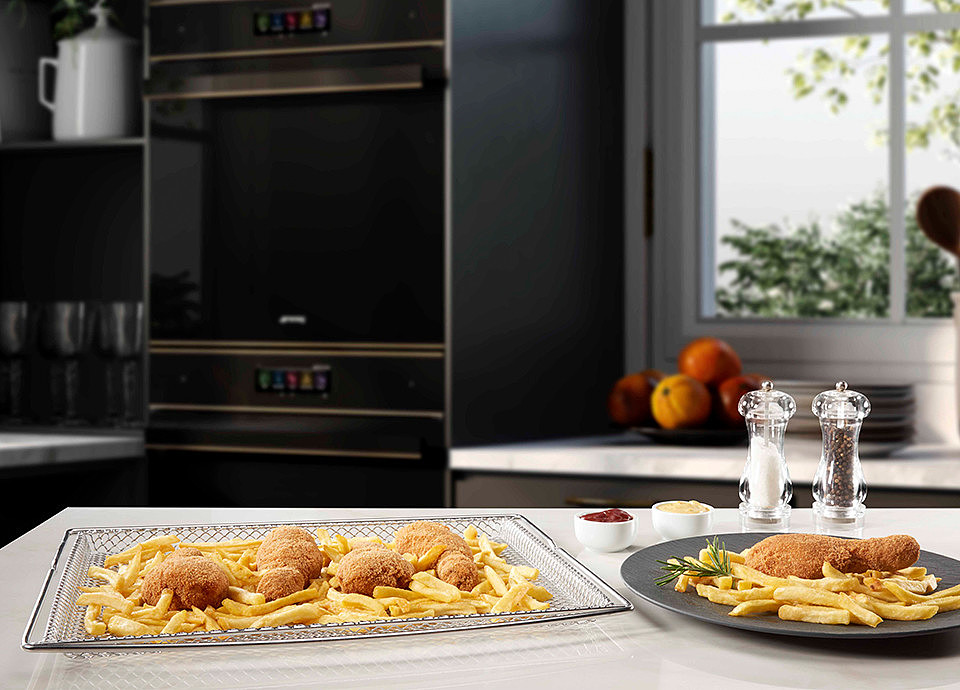 Una teglia airfry su un bancone da cucina con un piatto di cibo fritto e un piatto di patatine.